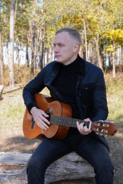 Sonbahar ormanında dışarıda gitar çalan sarışın bir adam. Ses terapisi, akıl sağlığı ve sağlık ayinleri kavramı. Sakinlik sükuneti ses duyusal uygulamaları. Aura tarım enerjisi bütünsel