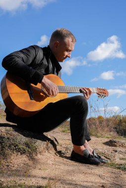 Sonbahar ormanında dışarıda gitar çalan sarışın bir adam. Ses terapisi, akıl sağlığı ve sağlık ayinleri kavramı. Sakinlik sükuneti ses duyusal uygulamaları. Aura tarım enerjisi bütünsel