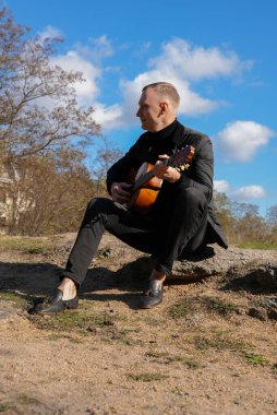 Sonbahar ormanında dışarıda gitar çalan sarışın bir adam. Ses terapisi, akıl sağlığı ve sağlık ayinleri kavramı. Sakinlik sükuneti ses duyusal uygulamaları. Aura tarım enerjisi bütünsel