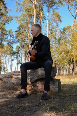 Gülümseyen beyaz ressamın portresi sonbahar parkında ahşap akustik gitar çalar. Genç söz yazarı, sonbahar zamanı dışarıda telli müzik aleti hobisi yapıyor. Sesli müzik doğal olarak iyileşir.