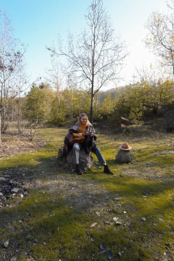 Sonbahar ormanında dışarıda gitar çalan sarışın bir kadın. Ses terapisi, akıl sağlığı ve sağlık ayinleri kavramı. Sakinlik sükuneti ses duyusal uygulamaları. Aura tarım enerjisi bütünsel