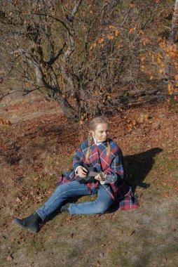 Sonbahar ormanlarında gitar çalan sarışın bir kadın var. Ses terapisi, akıl sağlığı ve sağlık ayinleri kavramı. Sakinlik sükuneti ses duyusal uygulamaları. Aura tarım enerjisi bütünsel