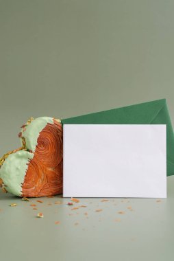 Zarflı tebrik kartı maketli boş bir şablon kağıdı. Fotokopi alanı olan yeşil arka planda kalp şeklinde şam fıstıklı kruvasan. Puf puf yeni moda tatlı pastanesi. Kremalı hamur