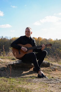 Sonbahar ormanında dışarıda gitar çalan sarışın bir adam. Ses terapisi, akıl sağlığı ve sağlık ayinleri kavramı. Sakinlik sükuneti ses duyusal uygulamaları. Aura tarım enerjisi bütünsel