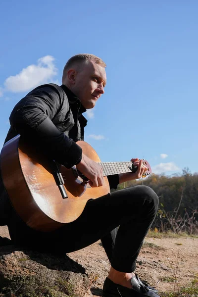 Gülümseyen beyaz ressamın portresi sonbahar parkında ahşap akustik gitar çalar. Genç söz yazarı, sonbahar zamanı dışarıda telli müzik aleti hobisi yapıyor. Sesli müzik doğal olarak iyileşir.