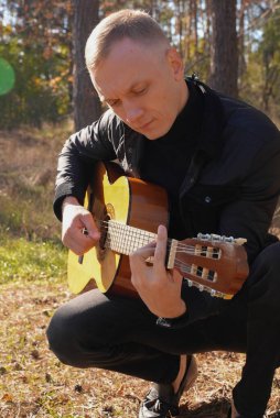 Sonbahar ormanında dışarıda gitar çalan sarışın bir adam. Ses terapisi, akıl sağlığı ve sağlık ayinleri kavramı. Sakinlik sükuneti ses duyusal uygulamaları. Aura tarım enerjisi bütünsel