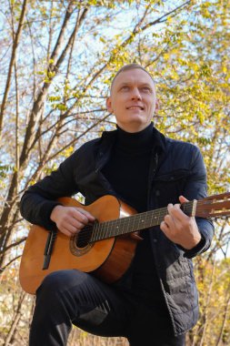 Sonbahar ormanında dışarıda gitar çalan sarışın bir adam. Ses terapisi, akıl sağlığı ve sağlık ayinleri kavramı. Sakinlik sükuneti ses duyusal uygulamaları. Aura tarım enerjisi bütünsel