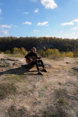 Sonbahar ormanında dışarıda gitar çalan sarışın bir adam. Ses terapisi, akıl sağlığı ve sağlık ayinleri kavramı. Sakinlik sükuneti ses duyusal uygulamaları. Aura tarım enerjisi bütünsel