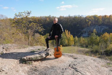 Güzel sarışın adam akustik gitar çalıyor ve şarkı söylüyor güneşli bir sonbahar gününde dışarıda eğleniyor. Sanatçı müzik aleti öğreniyor ve pratik yapıyor. Sonbahar mevsimsel havayı terk eder 