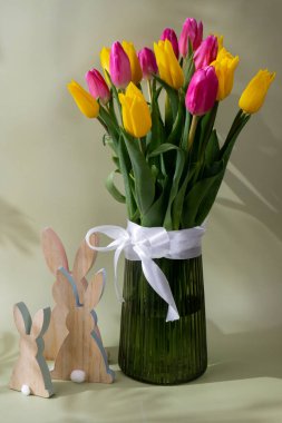 Mutlu Paskalya kompozisyonu ahşap tavşan. Renkli lale çiçeklerinden oluşan bir buket. Pastel arka planda gölgeler var. Bahar tatilleri için minimalist tasarım tebrik kartı. Paskalya hediyesi. Boşluğu kopyala
