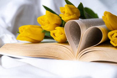 Kalp sembolü şeklinde kitap sayfaları dağınık yatakta pembe lale buketi ile aşk. Romantik sabah sahnesi. Tebrik kartı. Bahar zamanı çiçekleri.