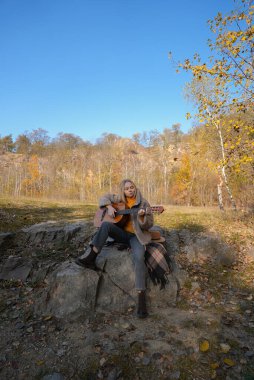 Sonbahar ormanında dışarıda gitar çalan sarışın bir kadın. Ses terapisi, akıl sağlığı ve sağlık ayinleri kavramı. Sakinlik sükuneti ses duyusal uygulamaları. Aura tarım enerjisi bütünsel