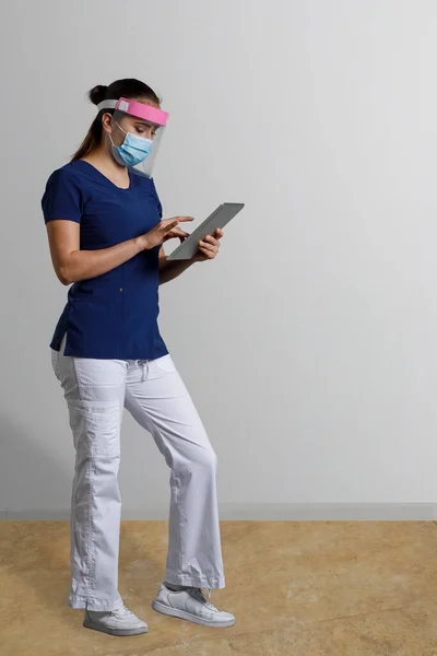 拉丁女人 身穿护士制服 头戴口罩 手里拿着一个数码平板电脑 灰色的背景上有文字的空间 — 图库照片