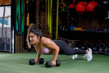 Chica latina joven haciendo ejercicios con pesas en gimnasio con ropa deportiva y cuerpo atltico.
