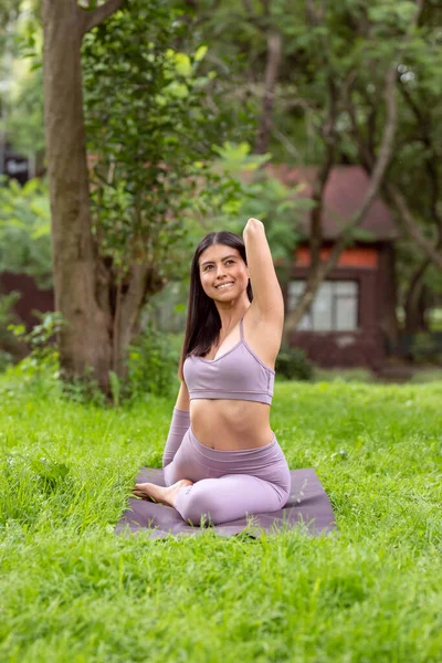 Latin woman doing Yoga-asanas with different postures, in the outdoor park with grass and trees in the background