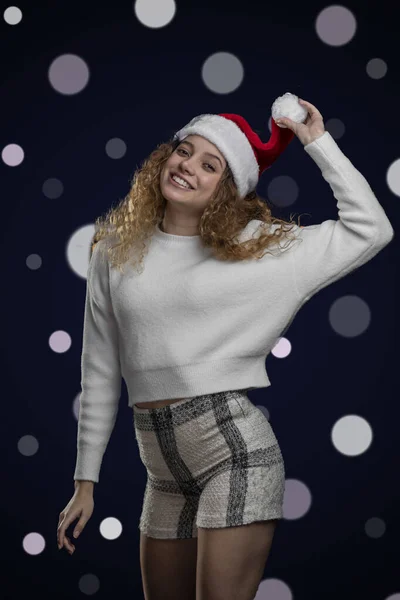 Fröhliches lateinisches Mädchen, das Weihnachten mit Weihnachtsmütze und einem Hintergrund mit defokussiertem Licht feiert, Platz für Text — Stockfoto