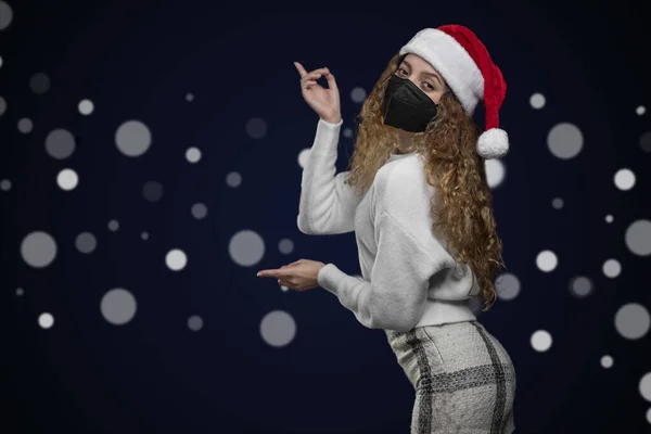 Lateinische Frau in Weihnachtskleidung mit Maske, die auf einen Raum für Werbetexte zeigt — Stockfoto