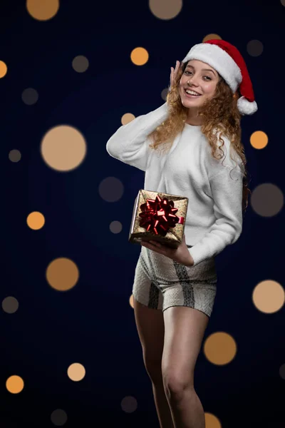 Junge Lateinerin lächelt und feiert Weihnachten mit einem Geschenk in der Hand und einem Nikolausmütze — Stockfoto