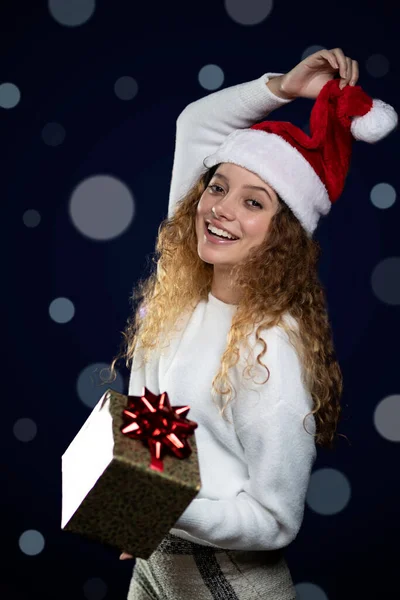 Junge lateinische Frau, die ein Weihnachtsgeschenk mit Weihnachtsmann-Hut zeigt. Raum für Text — Stockfoto