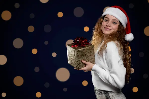 Junge lateinische Frau, die ein Weihnachtsgeschenk mit Weihnachtsmann-Hut zeigt. Raum für Text — Stockfoto