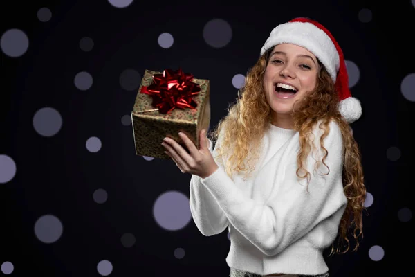 Junge lateinische Frau, die ein Weihnachtsgeschenk mit Weihnachtsmann-Hut zeigt. Raum für Text — Stockfoto