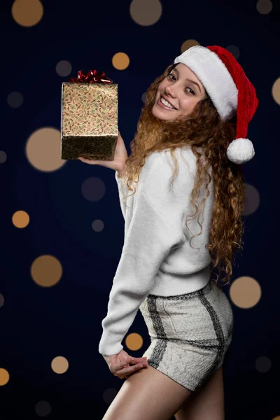 Junge lateinische Frau, die ein Weihnachtsgeschenk mit Weihnachtsmann-Hut zeigt. Raum für Text — Stockfoto