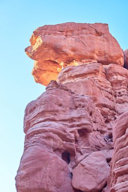 Görkemli kızıl kaya oluşumları, açık mavi gökyüzüne karşı yükselip doğanın sanatsal yapısının karmaşık dokularını ve renklerini vurgular.