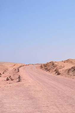 Tozlu yol, kayalık oluşumları ve parlak mavi gökyüzü ile kurak ve kurak bir arazide doğal güzellik ve sükuneti gözler önüne serer.