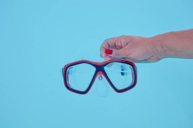 Bir el canlı bir dalış maskesi tutuyor, berrak lensler ve renkli bir çerçeve sergiliyor, parlak mavi bir arkaplanı var, su teması için mükemmel.