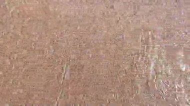 Su, kumlu sahilde sorunsuz bir şekilde akar ve çekilirken dalgalanmalar ve dokular yaratır. Bu da elementler arasındaki dinamik etkileşimi gösterir.