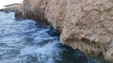 Dalgalar sürekli olarak kayalık kıyı şeridine çarpar köpük ve su sıçratır su ve kayanın dinamik etkileşimini gösterir.