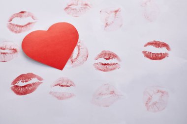 Kırmızının tonlarında çeşitli ruj izi olan beyaz kağıda yerleştirilmiş kırmızı bir kalp şekli romantik bir tema oluşturuyor.