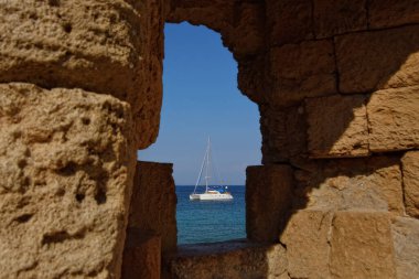Eski kalenin yıkıntılarının arasından tekneye bak. Güneşli güzel bir gün. Rodos Adası, Yunanistan