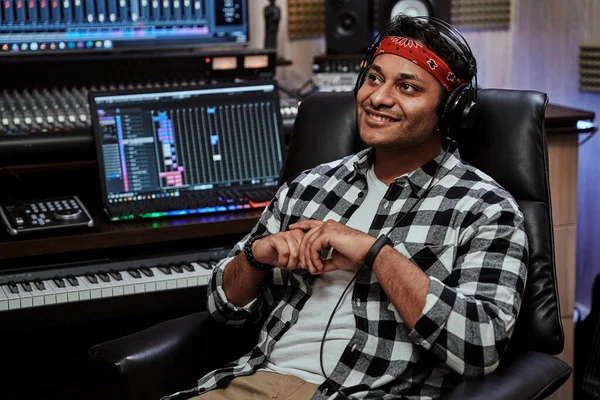 Retrato de jovem feliz, artista masculino em fones de ouvido sorrindo ao lado enquanto sentado no estúdio de gravação — Fotografia de Stock
