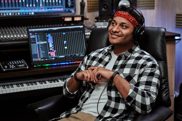 Portrait of happy young man, male artist in headphones smiling aside while sitting in recording studio