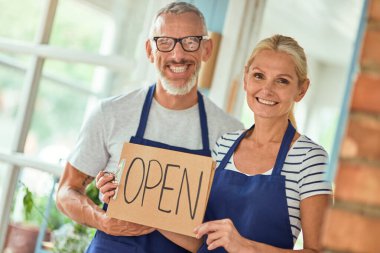 Orta yaşlı Kafkas eşleri açık dükkan tabelası taşıyorlar