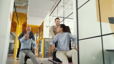Neşeli iş ekibi başarıyı kutluyor. Ofis koridorunda sandalye süren, gülen, bağıran ve eğlenen dört çılgın iş arkadaşı.