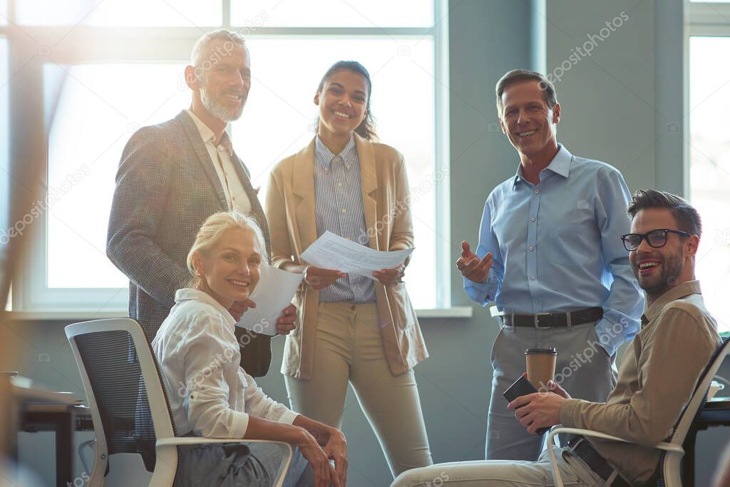 Strong and successful team. Group of happy multiracial business people smiling at camera while having a meeting at office