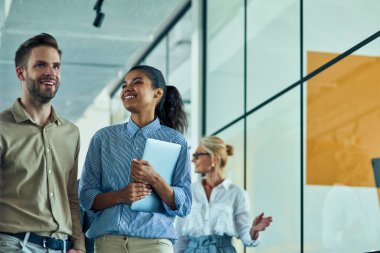 Genç neşeli melez kadın dizüstü bilgisayarını tutuyor ve iş toplantısından sonra modern ofiste dururken erkek arkadaşıyla konuşuyor.