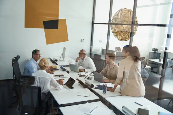 Ryhmä monirotuisia liikemiehiä, jotka jakavat ajatuksia ja keskustelevat projektista kokoushuoneessa työskennellessään yhdessä modernissa toimistossa — kuvapankkivalokuva