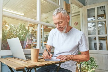 Orta yaşlı beyaz iş adamı laptopun yanında çalışıyor.