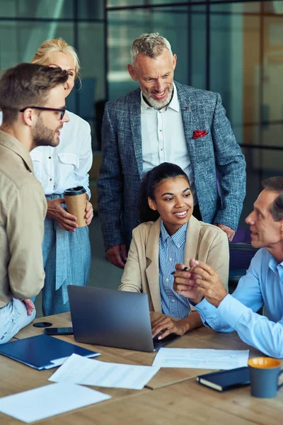 Fröhliches multiethnisches Businessteam mit Laptop, bespricht Projektergebnisse und lächelt bei einem Meeting im modernen Büro, arbeitet zusammen — Stockfoto