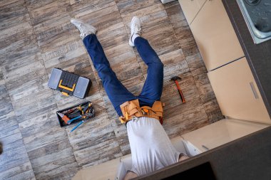 Young repairman lying on floor next to instruments