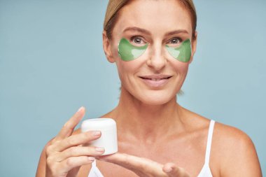 Mutlu, olgun bir bayan kameraya bakıyor ve cilt bakımını seviyor.