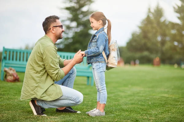Полнометражный снимок счастливого молодого отца, держащего дочерей за руки, папочку, проводящего время со своей милой маленькой девочкой в зеленом парке в теплый день — стоковое фото