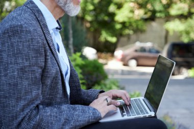 Herhangi bir yerde. Olgun iş adamı gündüz vakti dışarıda otururken dizüstü bilgisayarda çalışıyor.