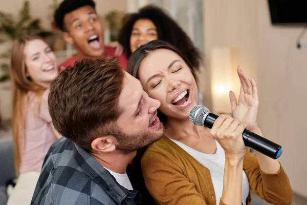Bernyanyi bersama. Pasangan muda yang bersemangat atau teman-teman memegang mikrofon dan bernyanyi bersama sambil bermain karaoke dengan teman-teman di rumah. Kelompok orang bersenang-senang di karaoke rumah pesta — Stok Foto