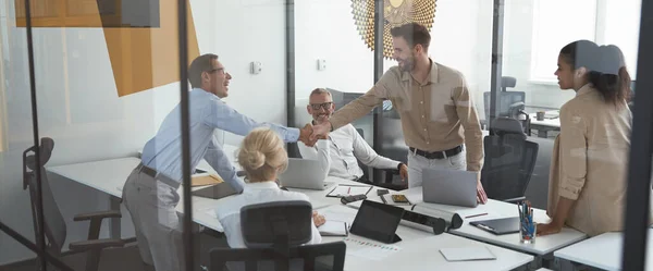 Zwei erfolgreiche Geschäftsleute beim Händeschütteln während eines Treffens mit Kollegen im Konferenzraum des modernen Büros — Stockfoto