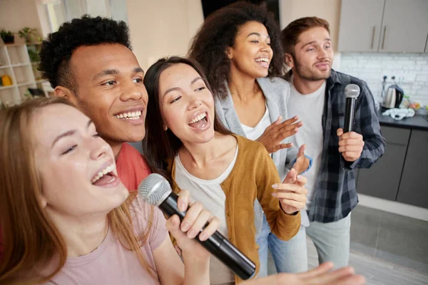 Musik seumur hidup. Happy multikultur teman-teman bernyanyi dengan mikrofon saat bermain karaoke di rumah, berdiri di apartemen modern — Stok Foto