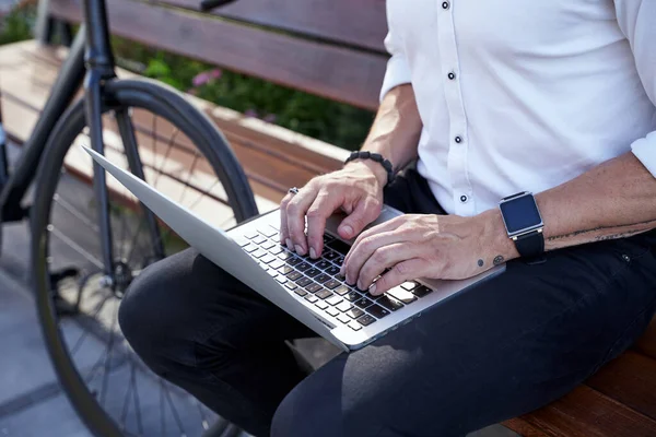 Pekerja sibuk. Potret modern usia pertengahan pengusaha berbaju putih bekerja pada laptop sambil duduk di bangku luar dengan sepeda di sampingnya — Stok Foto